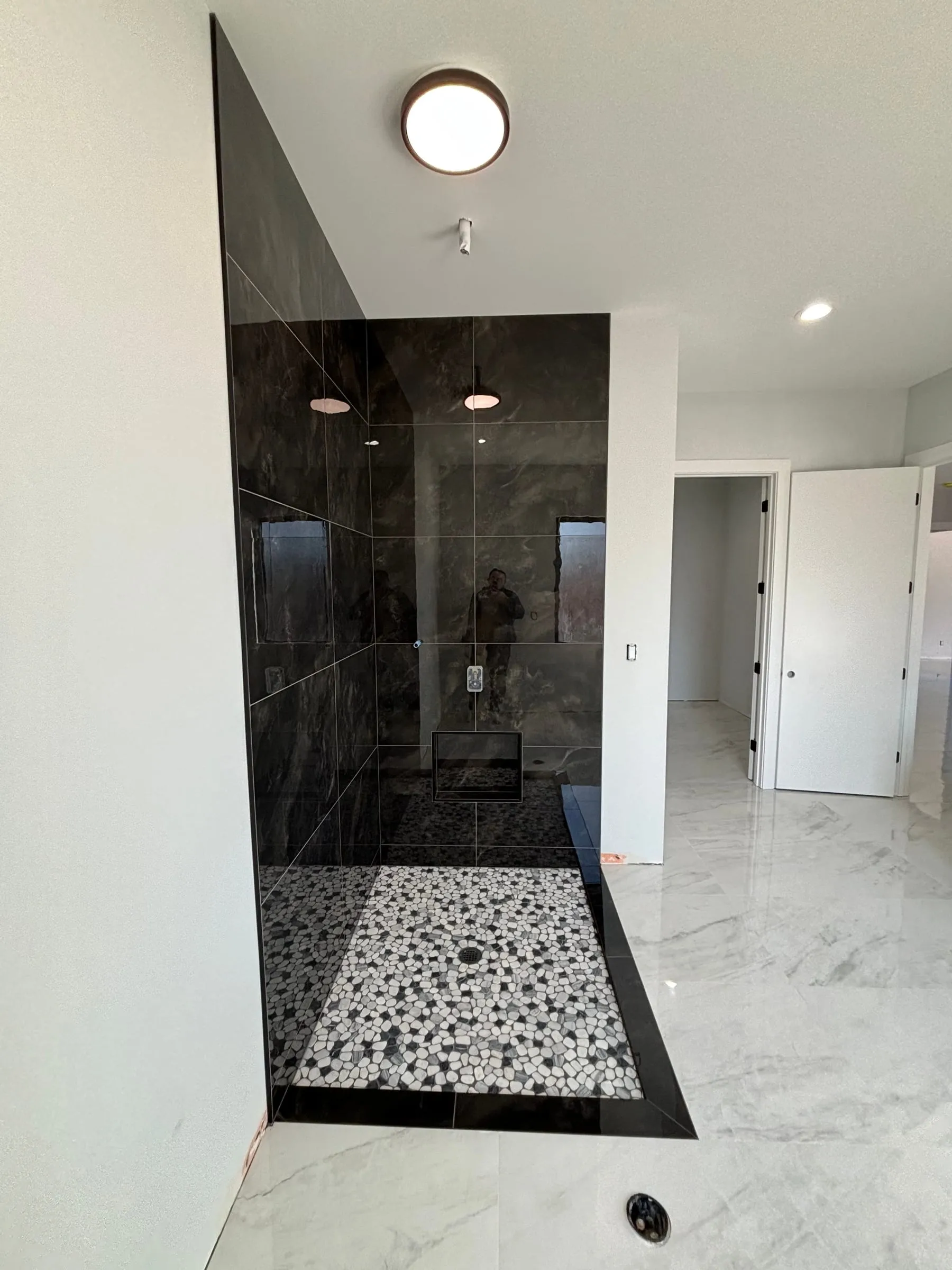 Shower with large black tile walls and a black and white pebble floor