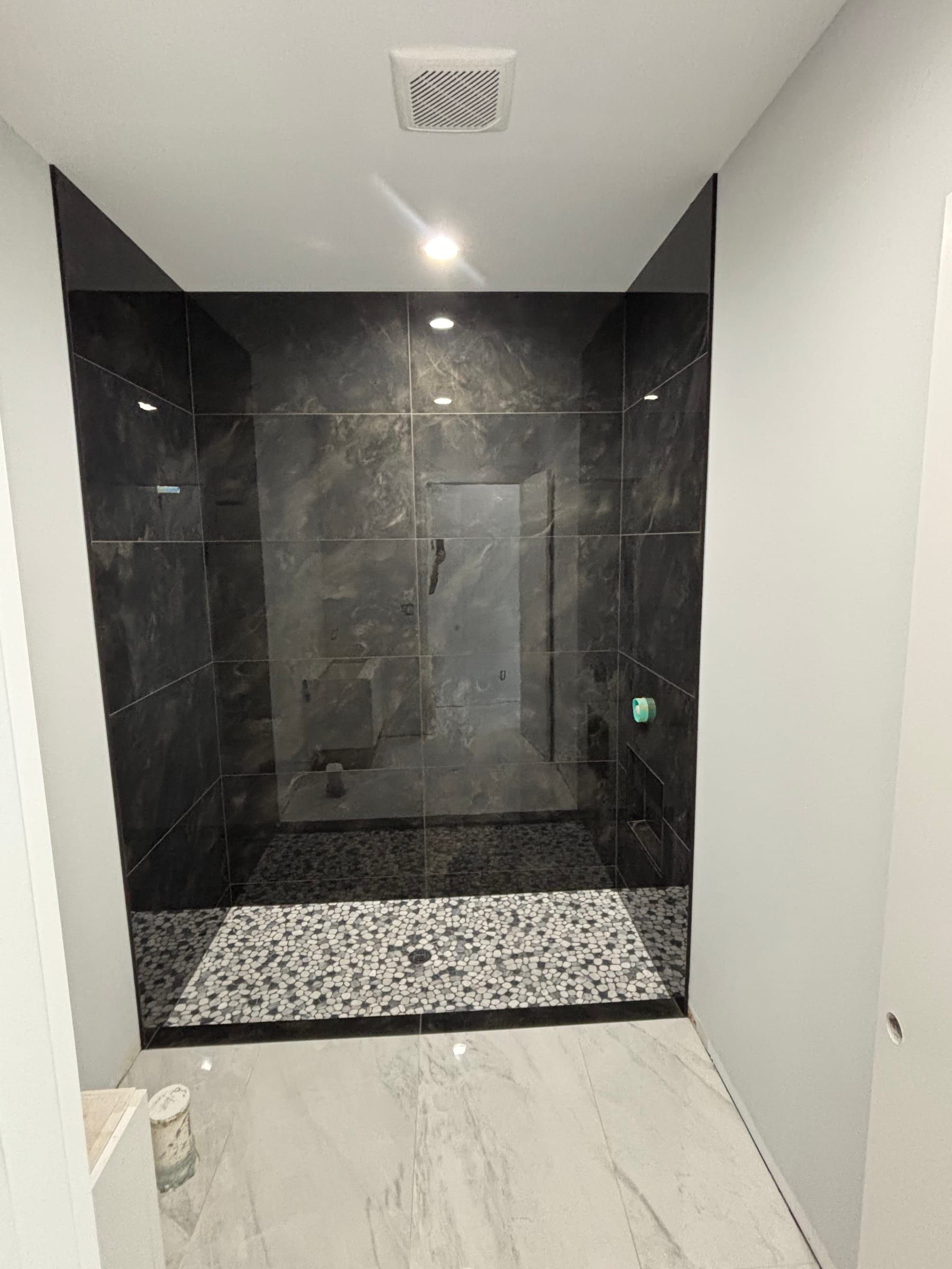 Black large-format shower with a pebble floor and a glossy marble-look bathroom floor