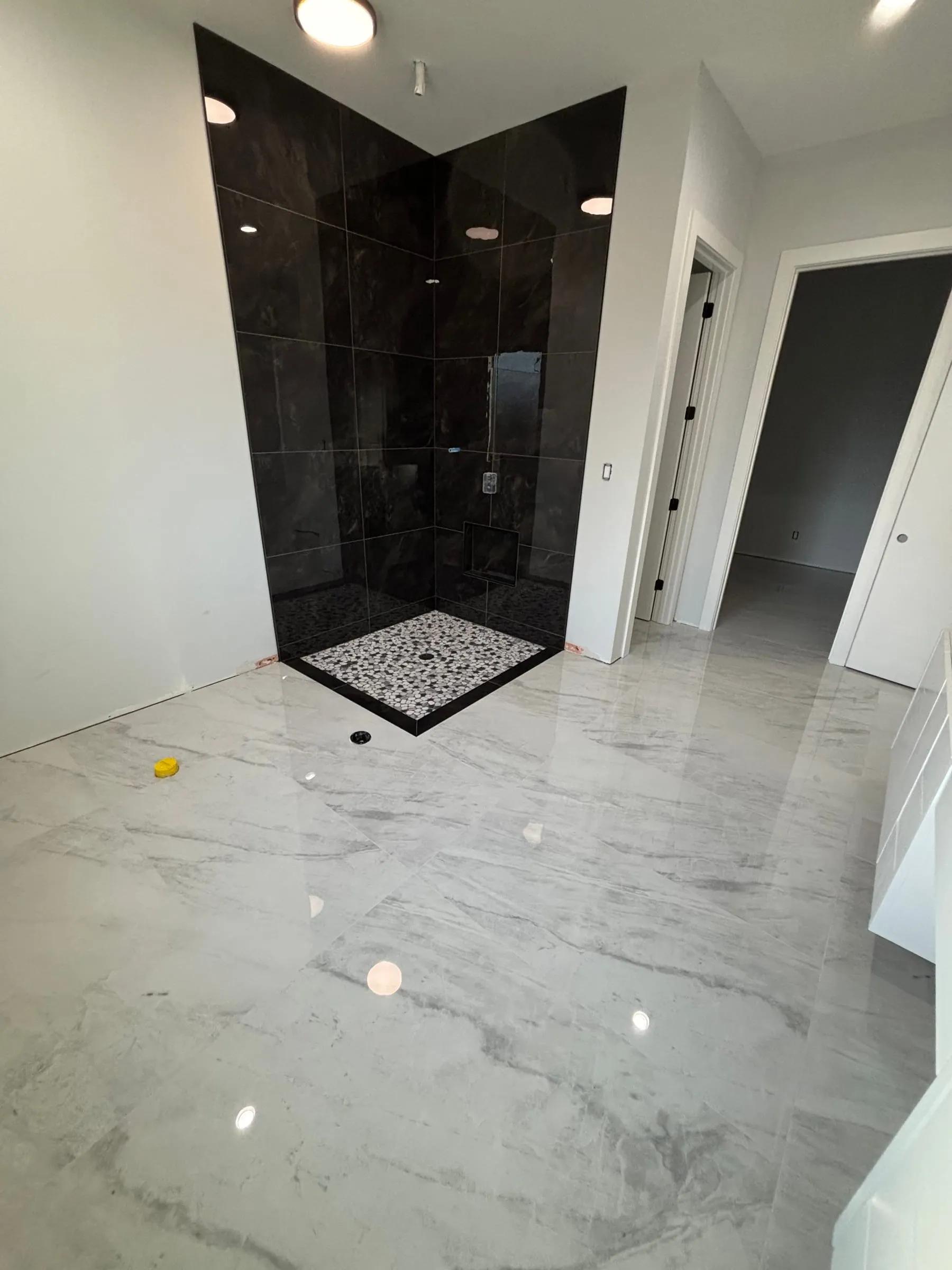 Bathroom floor in polished marble-look porcelain leading to the black shower