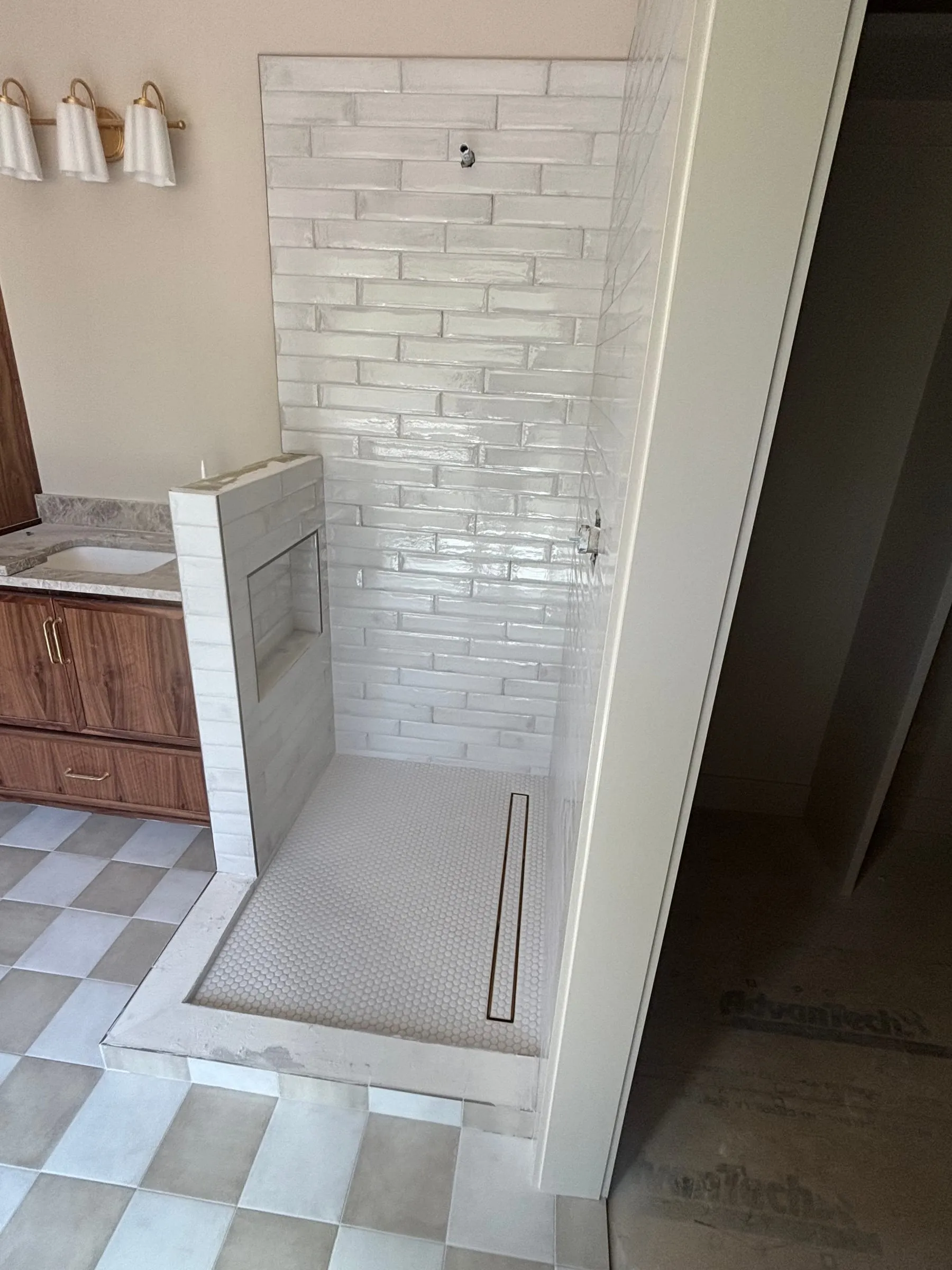 Curbless shower with a linear drain, glossy white subway walls, and a checkerboard floor