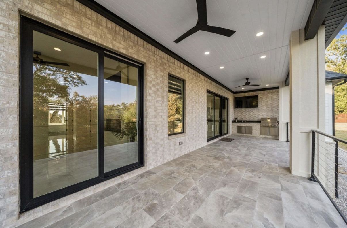Covered porch with large gray porcelain floor tile, sliding glass doors, and a stone wall