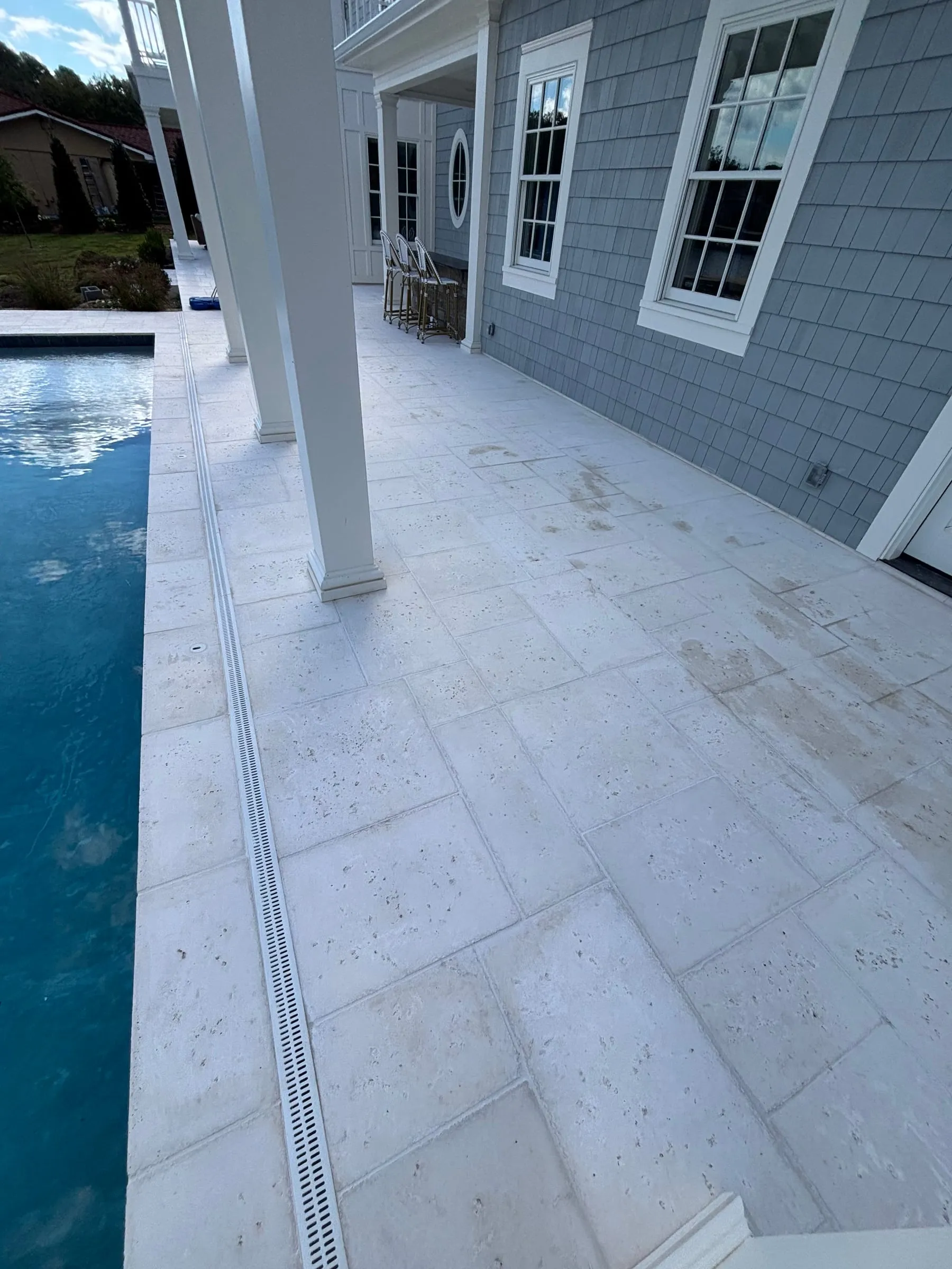 Pool deck in white travertine-look pavers with a linear drain along a covered porch