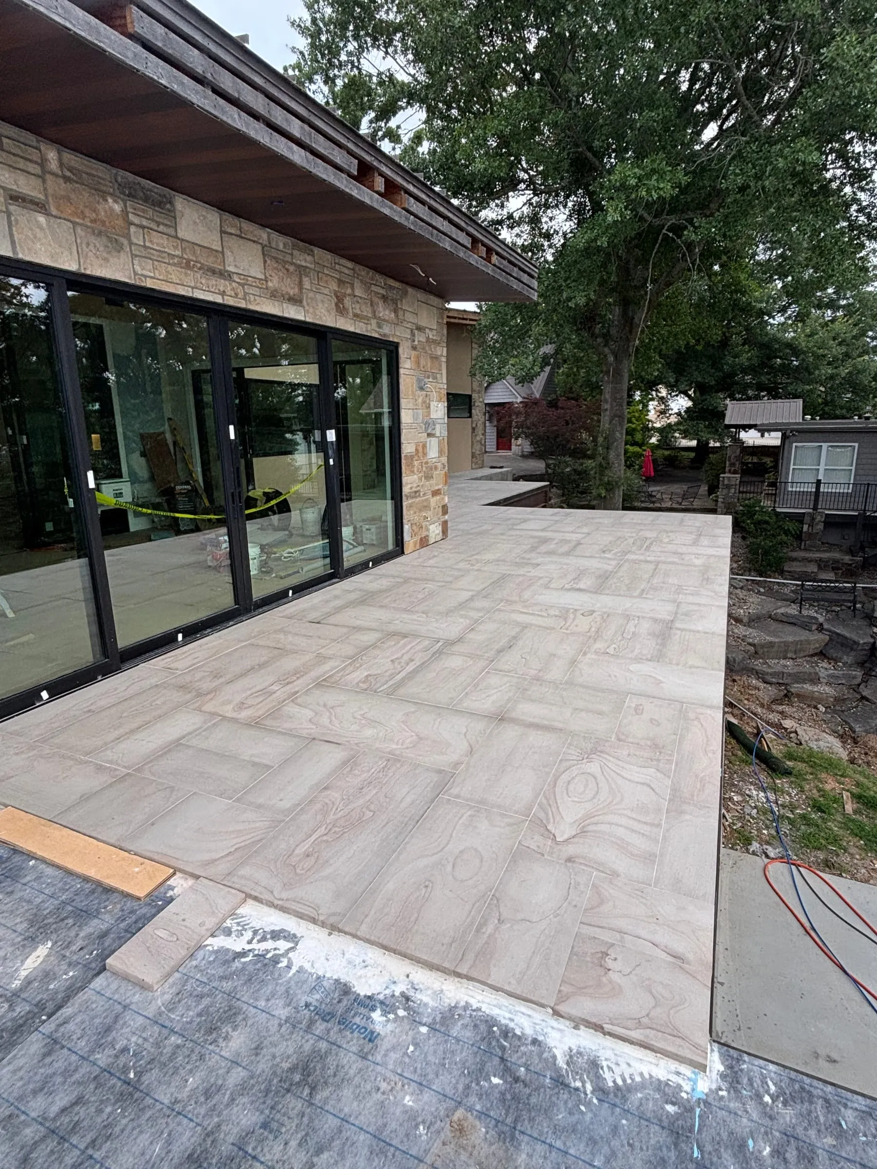 Large-format porcelain patio outside a wall of glass doors, during installation