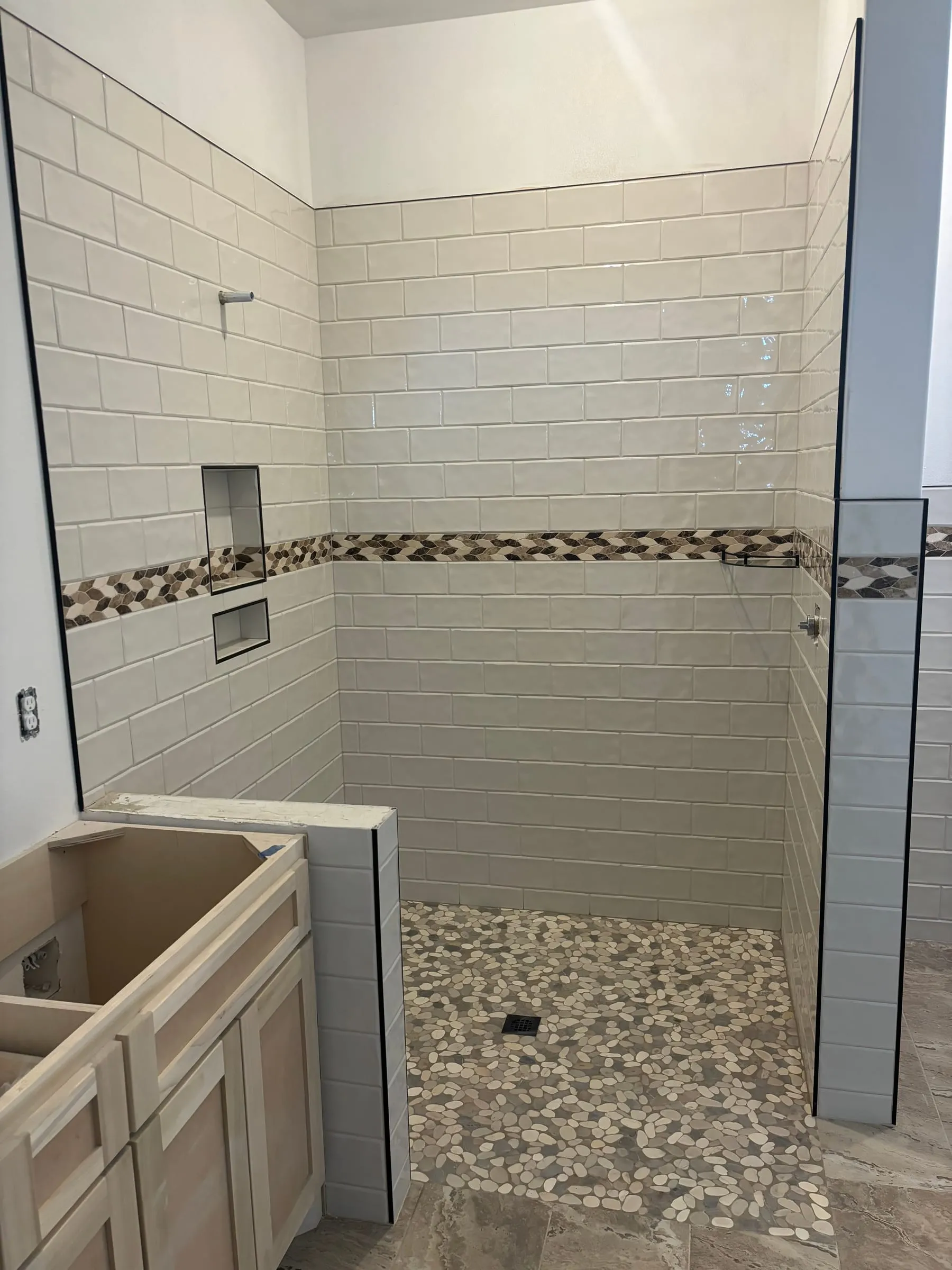 Walk-in shower in white subway tile with a diamond mosaic accent band and a pebble floor