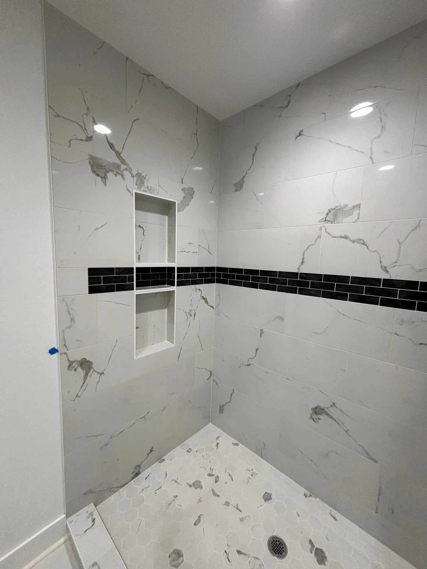 Marble-look shower with a black accent band, recessed niche, and matching floor
