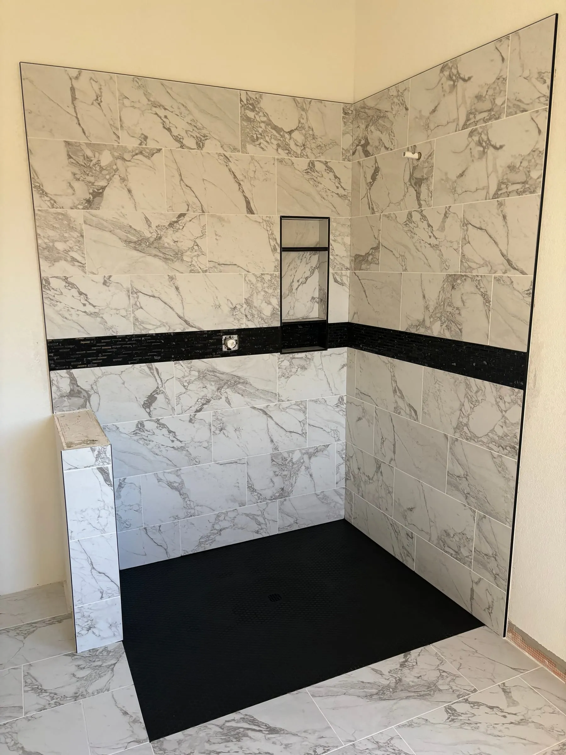 Marble-look shower walls with a black accent stripe and niche over a black shower floor