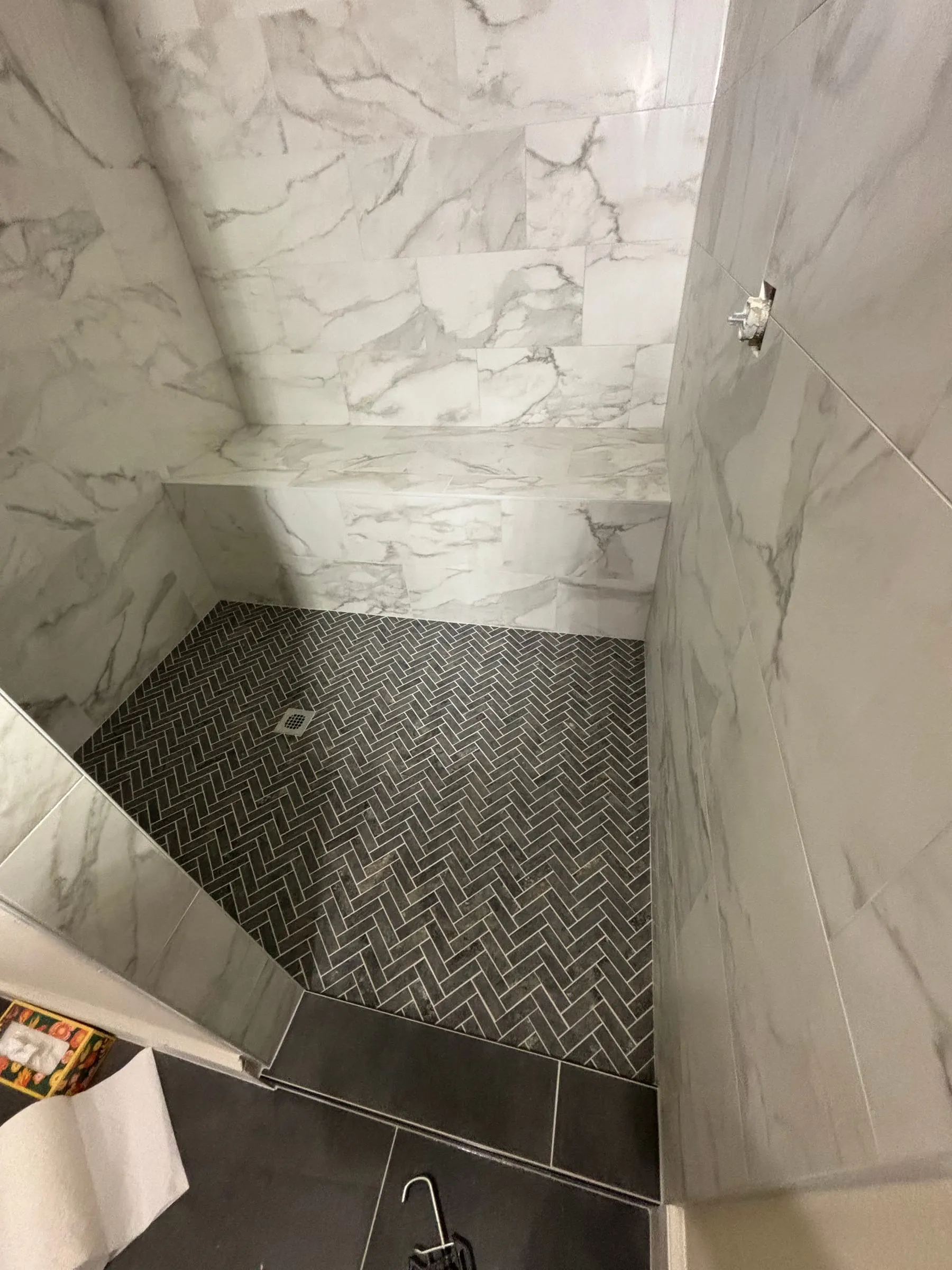Shower with marble-look walls, a tiled bench, and a black herringbone mosaic floor