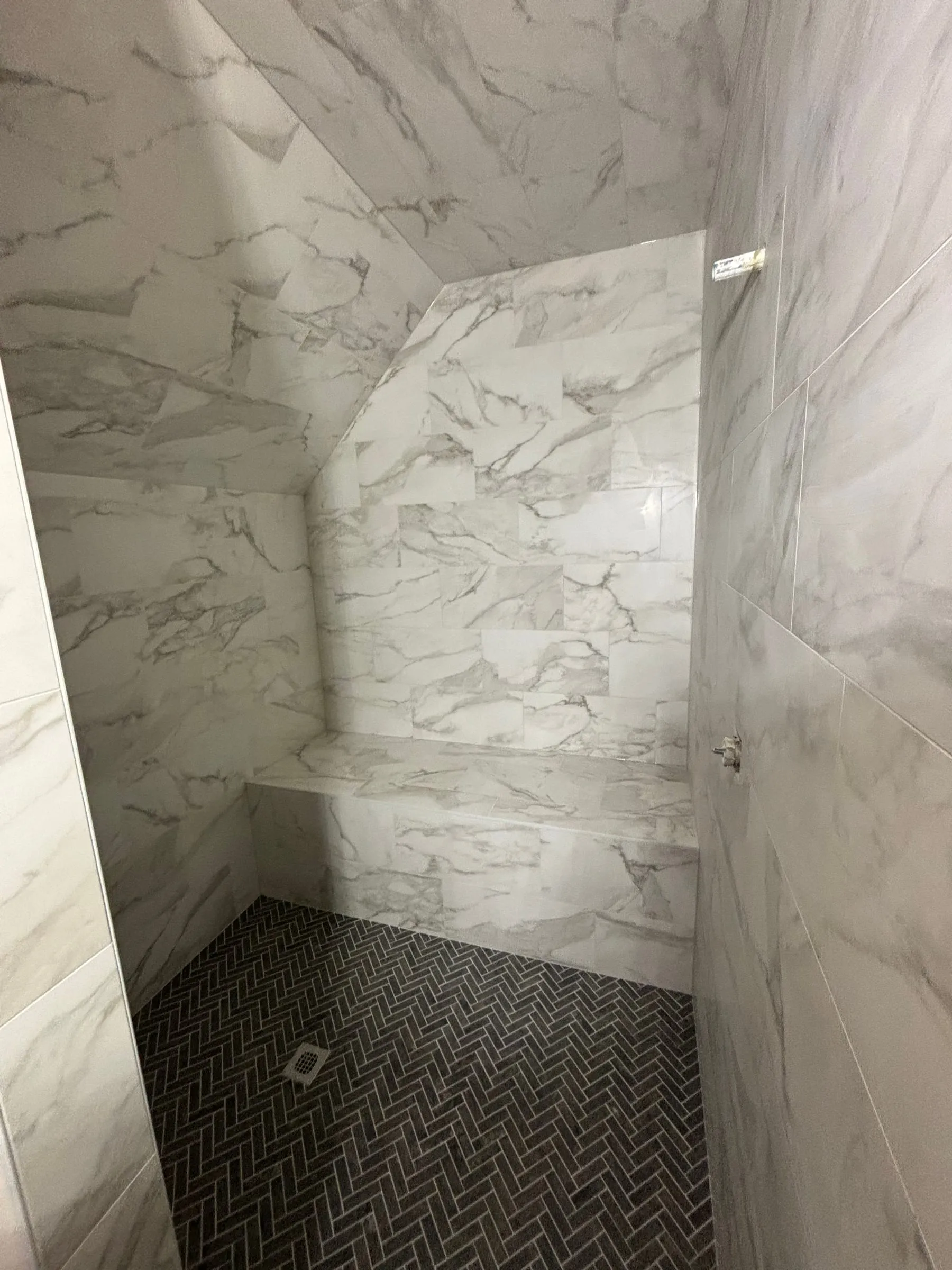 Black herringbone shower floor below marble-look walls and a tiled bench