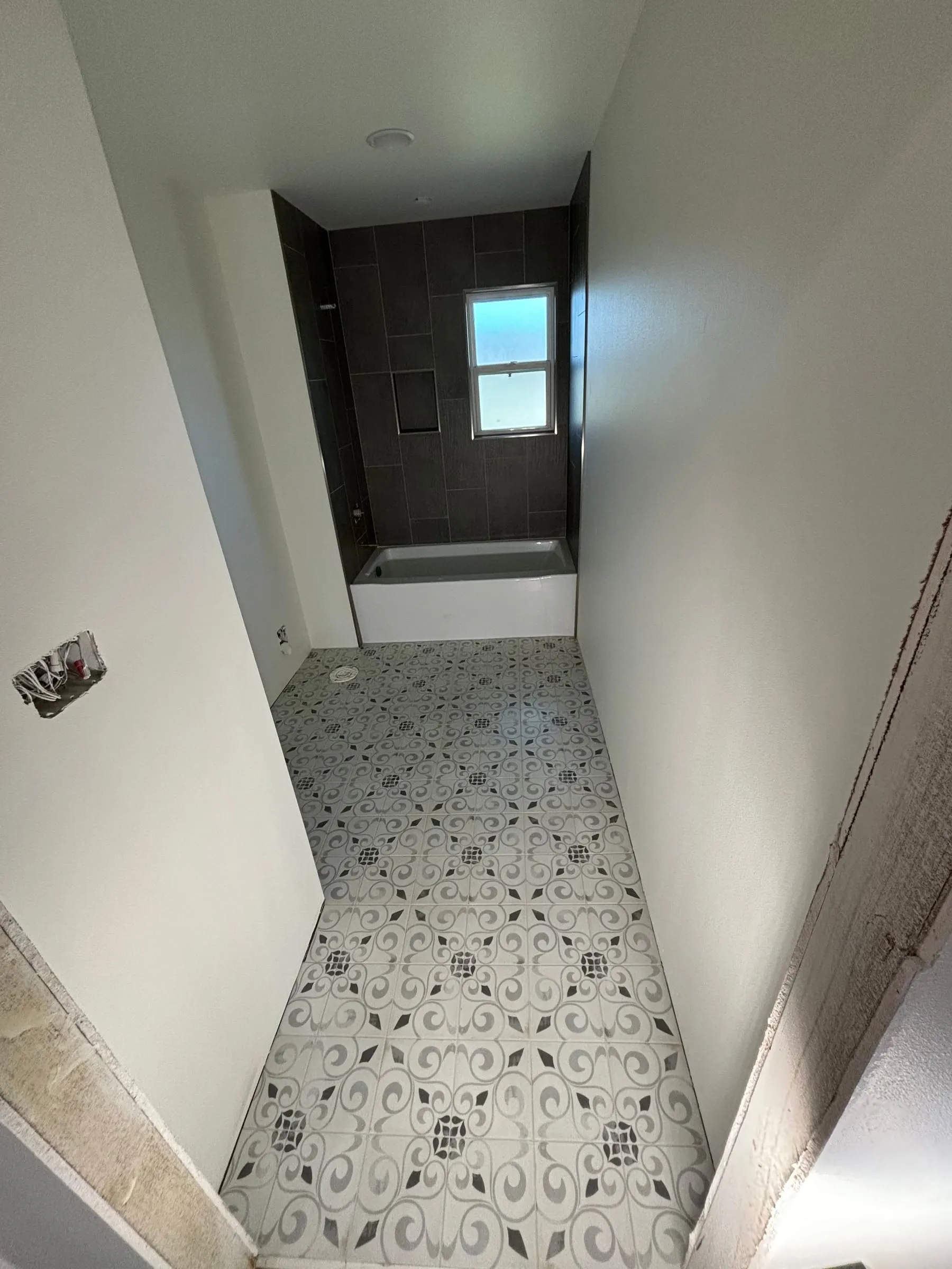 Bathroom with a patterned gray and white floor tile and a dark tiled tub wall
