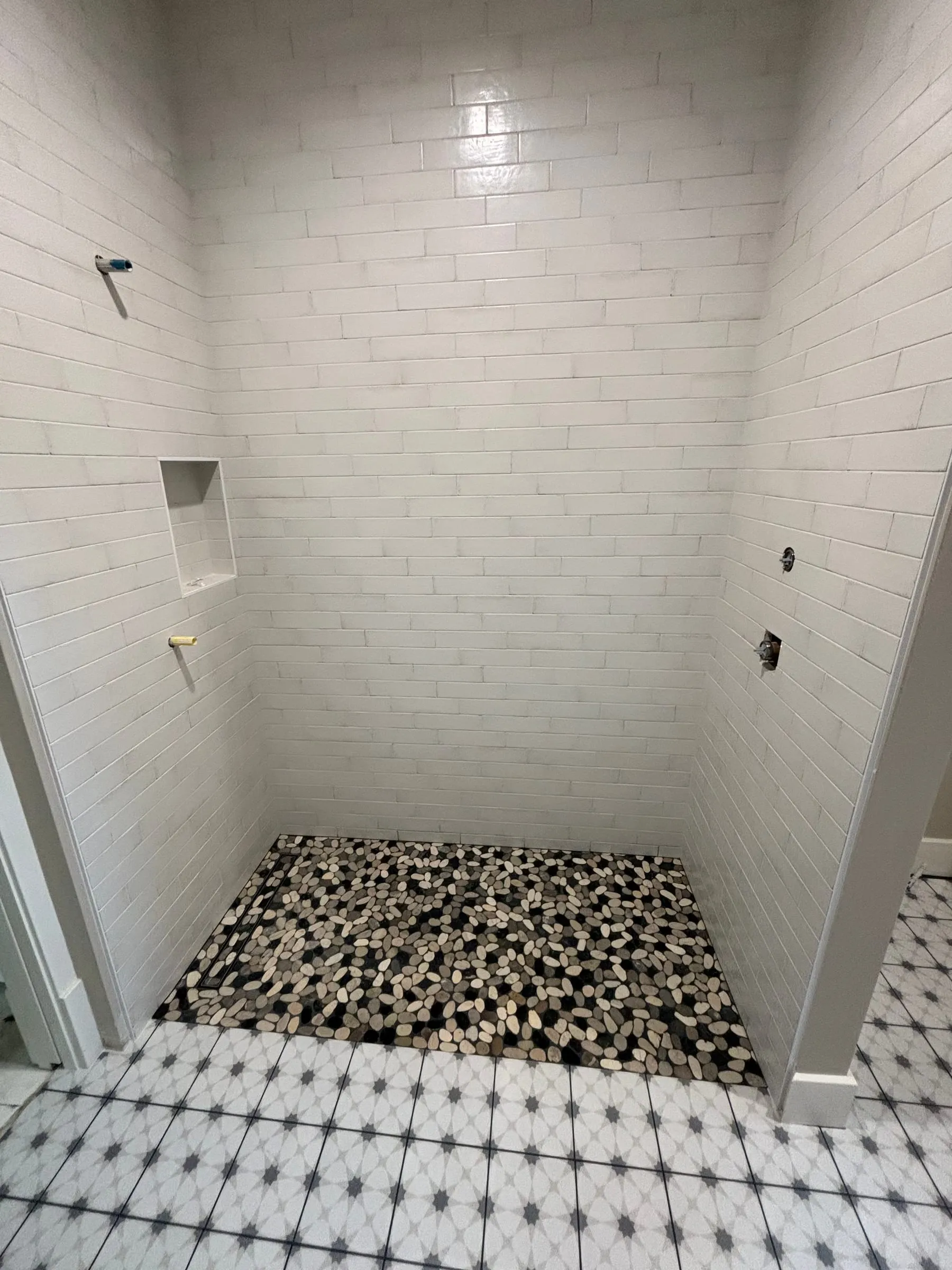 Shower in white subway tile with a black and white pebble floor