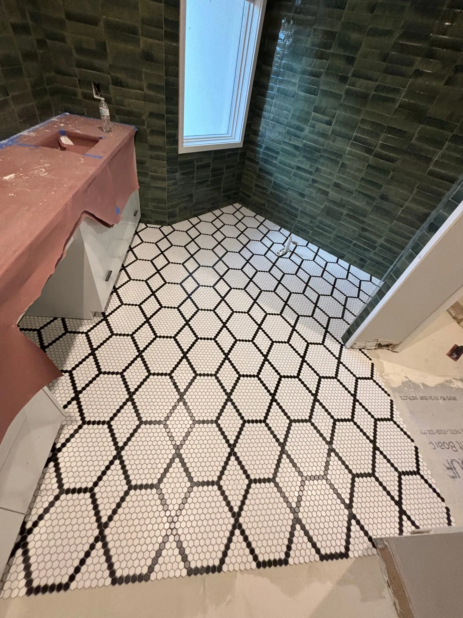 Bathroom with a white hexagon mosaic floor outlined in black and glossy green wall tile