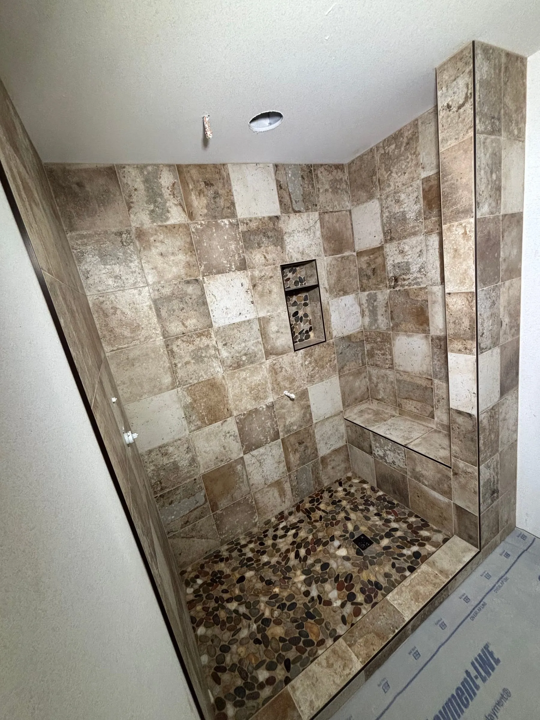 Walk-in shower in travertine-look square tile with a bench, niche, and river-rock floor