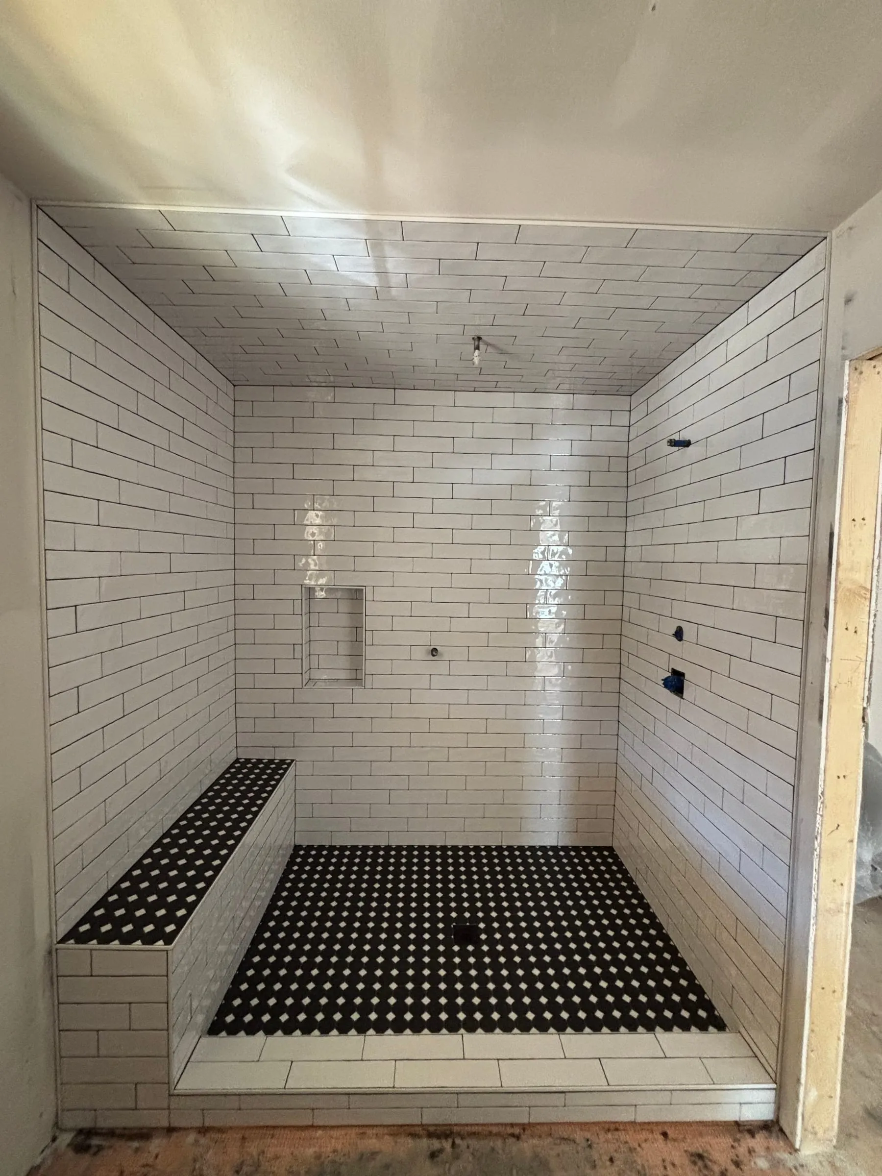 Glossy white subway tile shower with a tiled ceiling, bench, and black dot mosaic floor