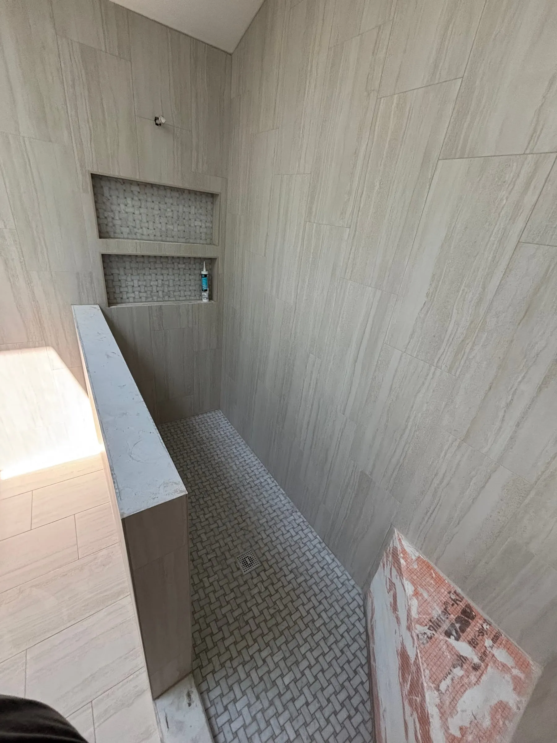Shower in large wood-look tile with double niches, a bench, and a basketweave mosaic floor