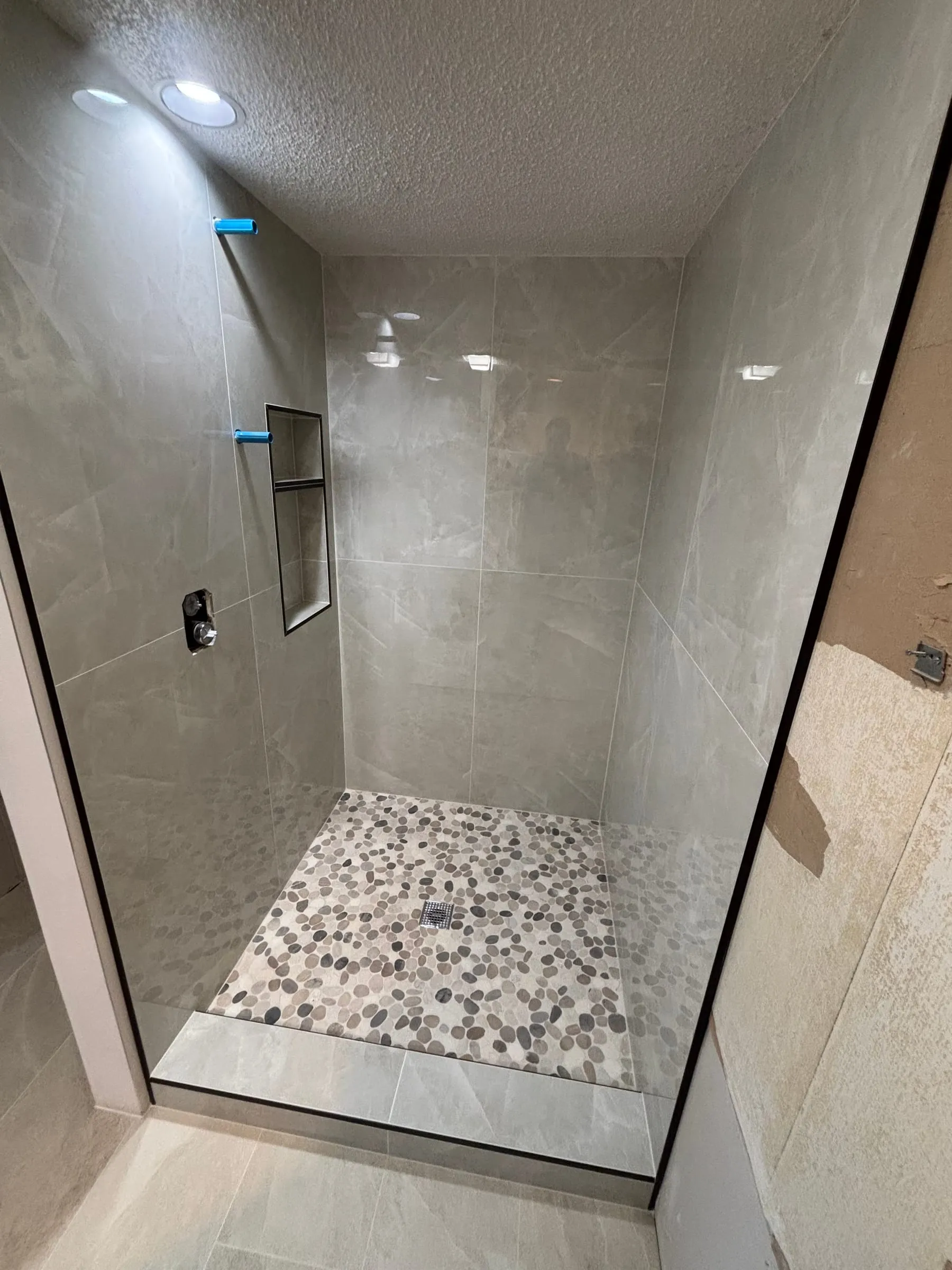 Glass-enclosed shower in large beige tile with a pebble floor and recessed niche