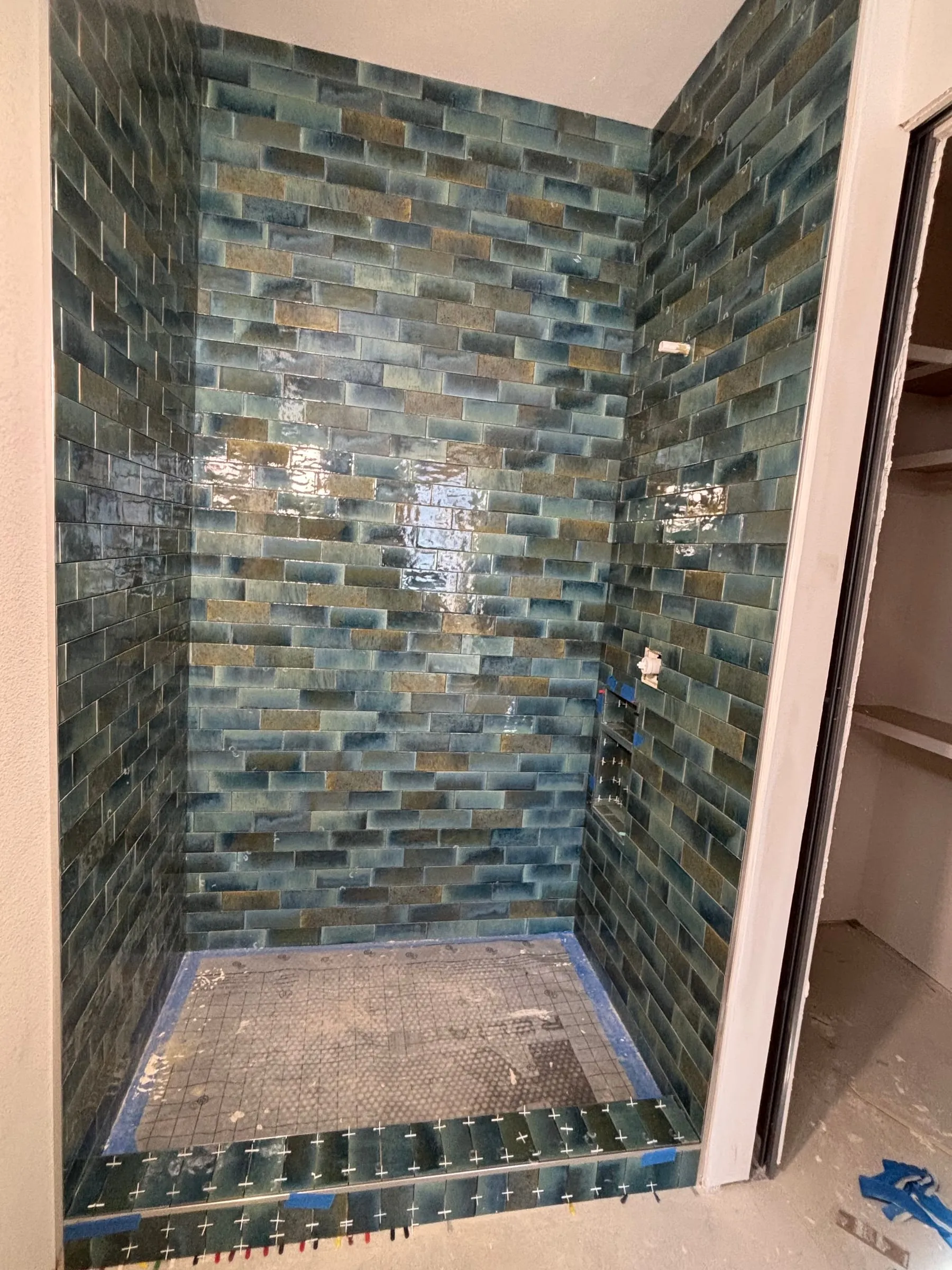 Shower walls in glossy blue and amber glass-look tile, during installation