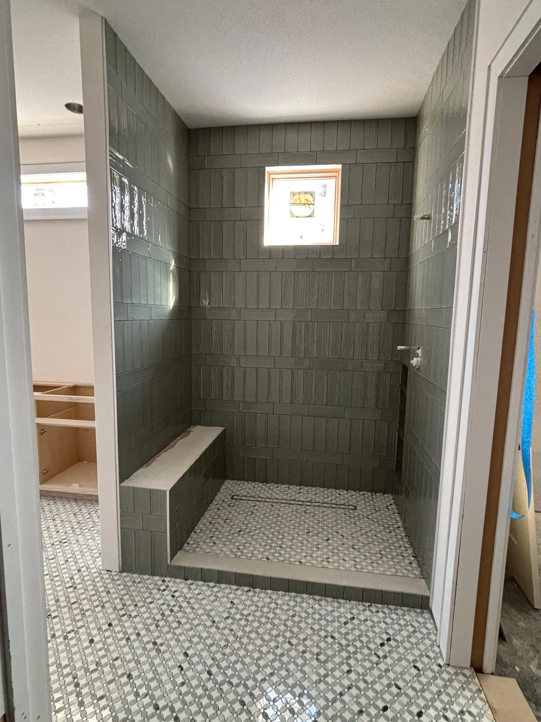 Shower in sage-green vertical tile with a bench, linear drain, and mosaic floor