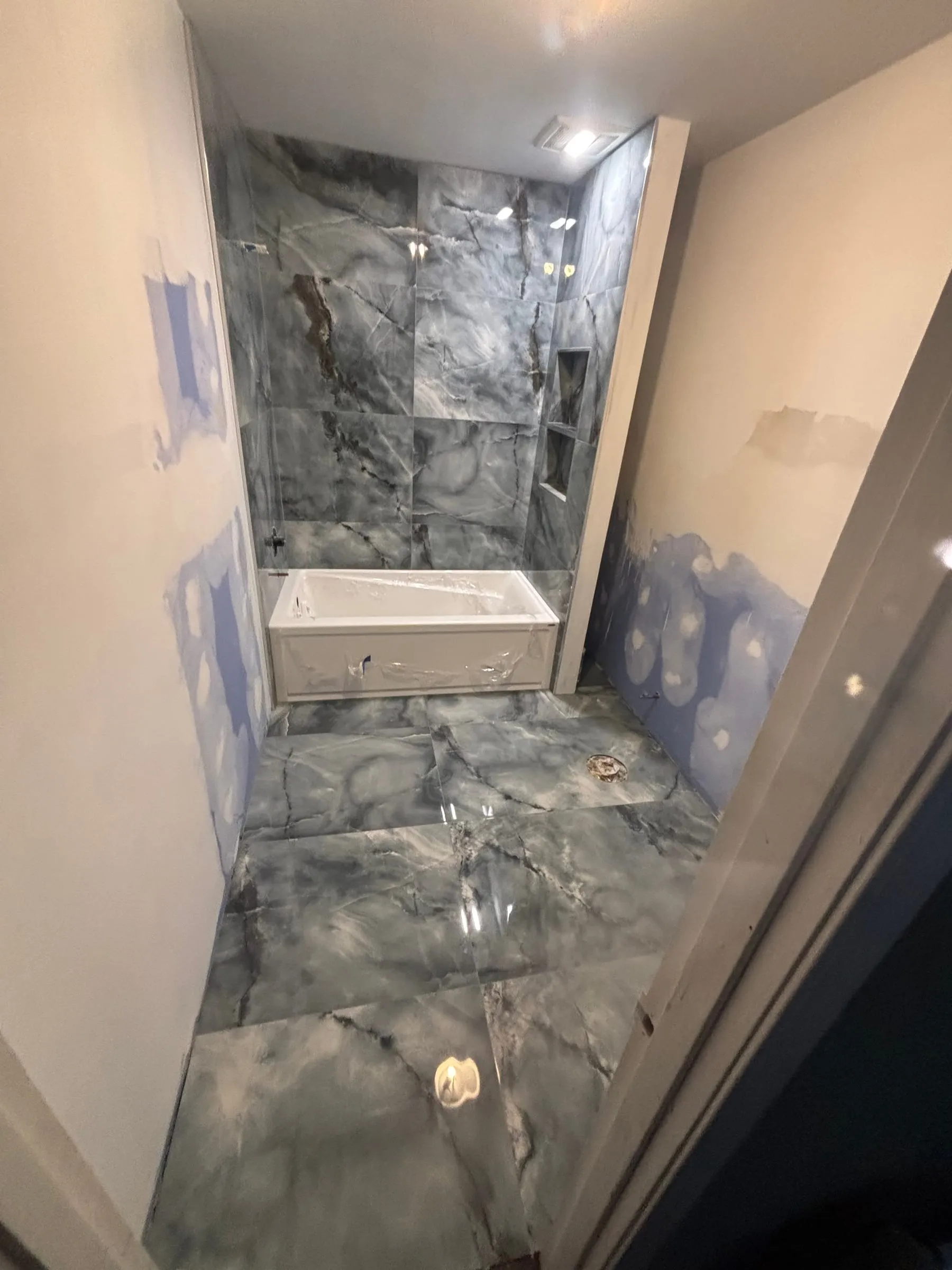 Tub surround and floor in glossy gray onyx-look large-format tile, during installation