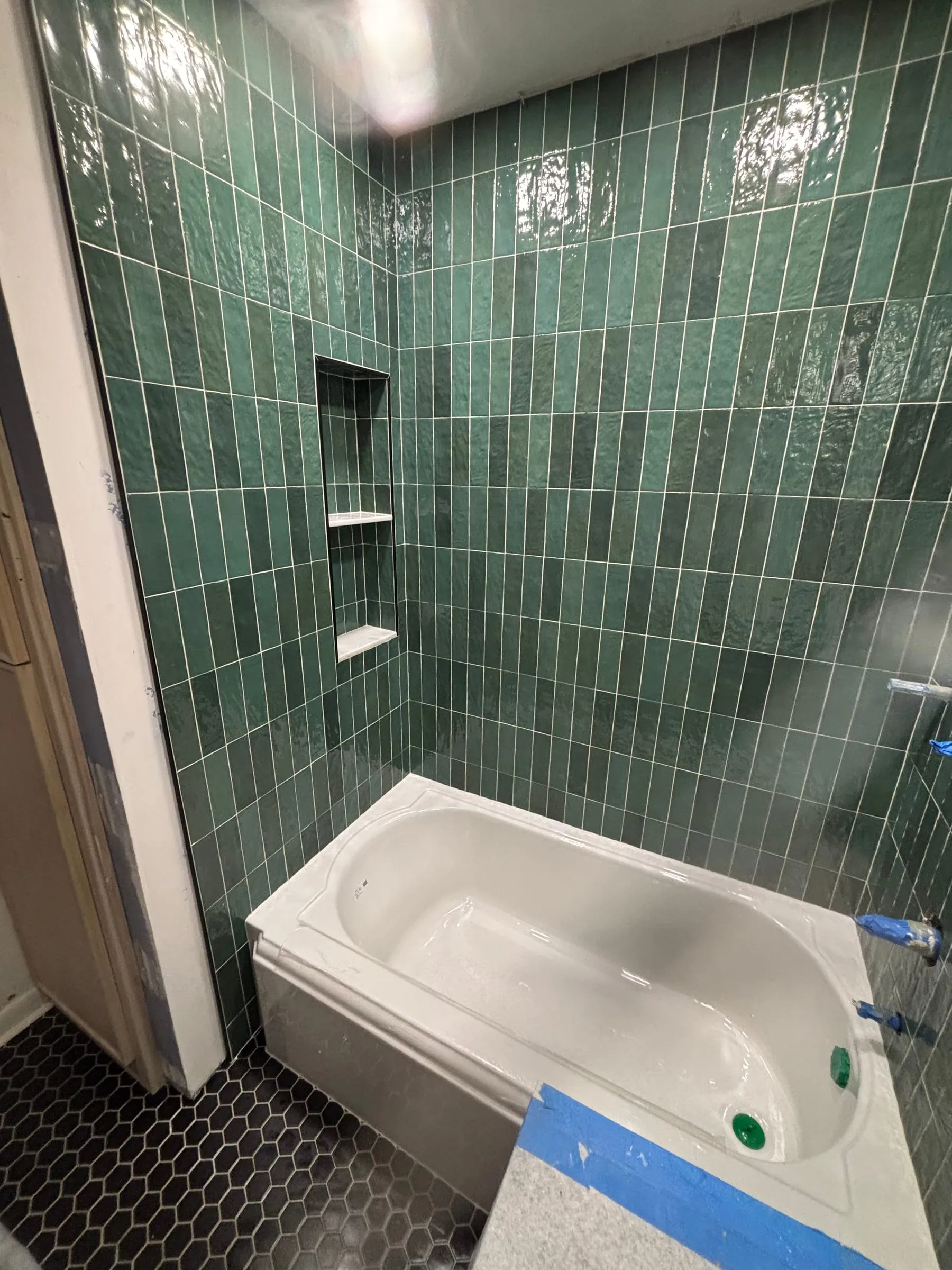 Tub surround in glossy green vertical tile with decorative accent tiles and a black hex floor