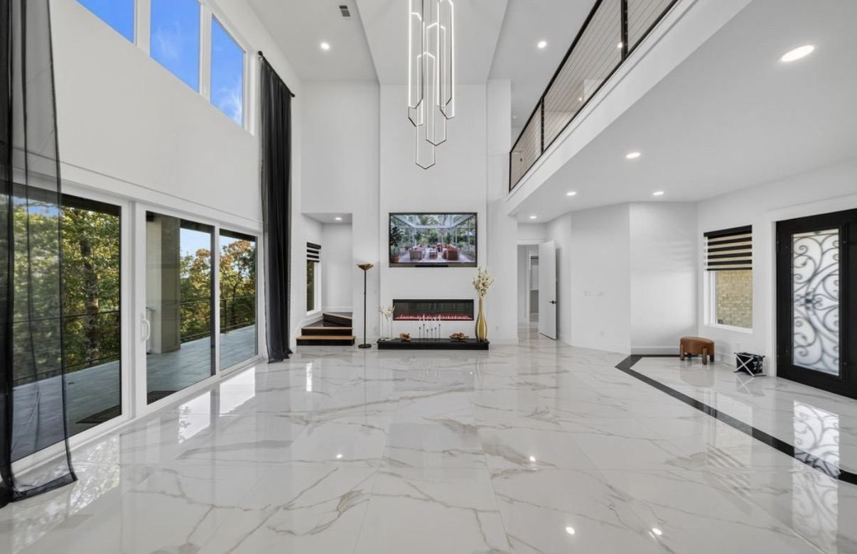 Two-story great room with large-format white marble-look porcelain floor and a black border band