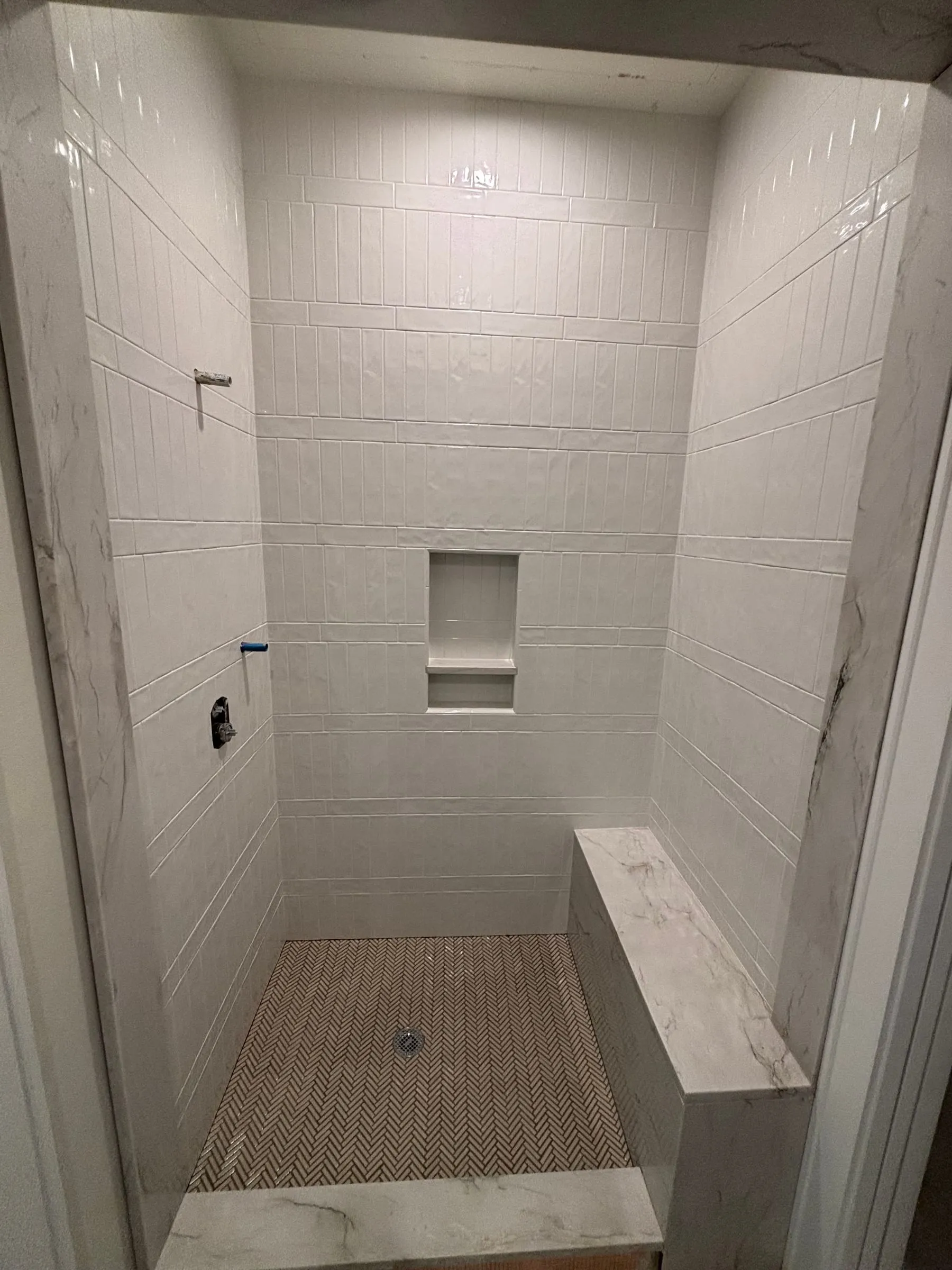 Walk-in shower in large white tile with a recessed niche, a bench, and a mosaic floor