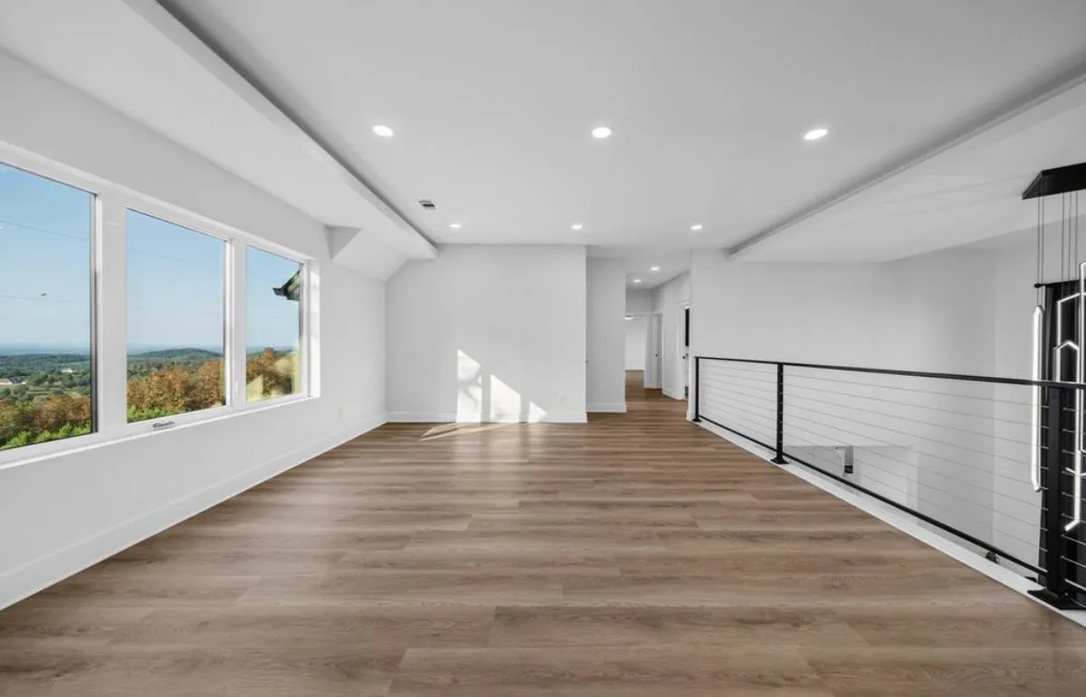 Upstairs loft with wood-look plank flooring, cable railing, and a wall of windows