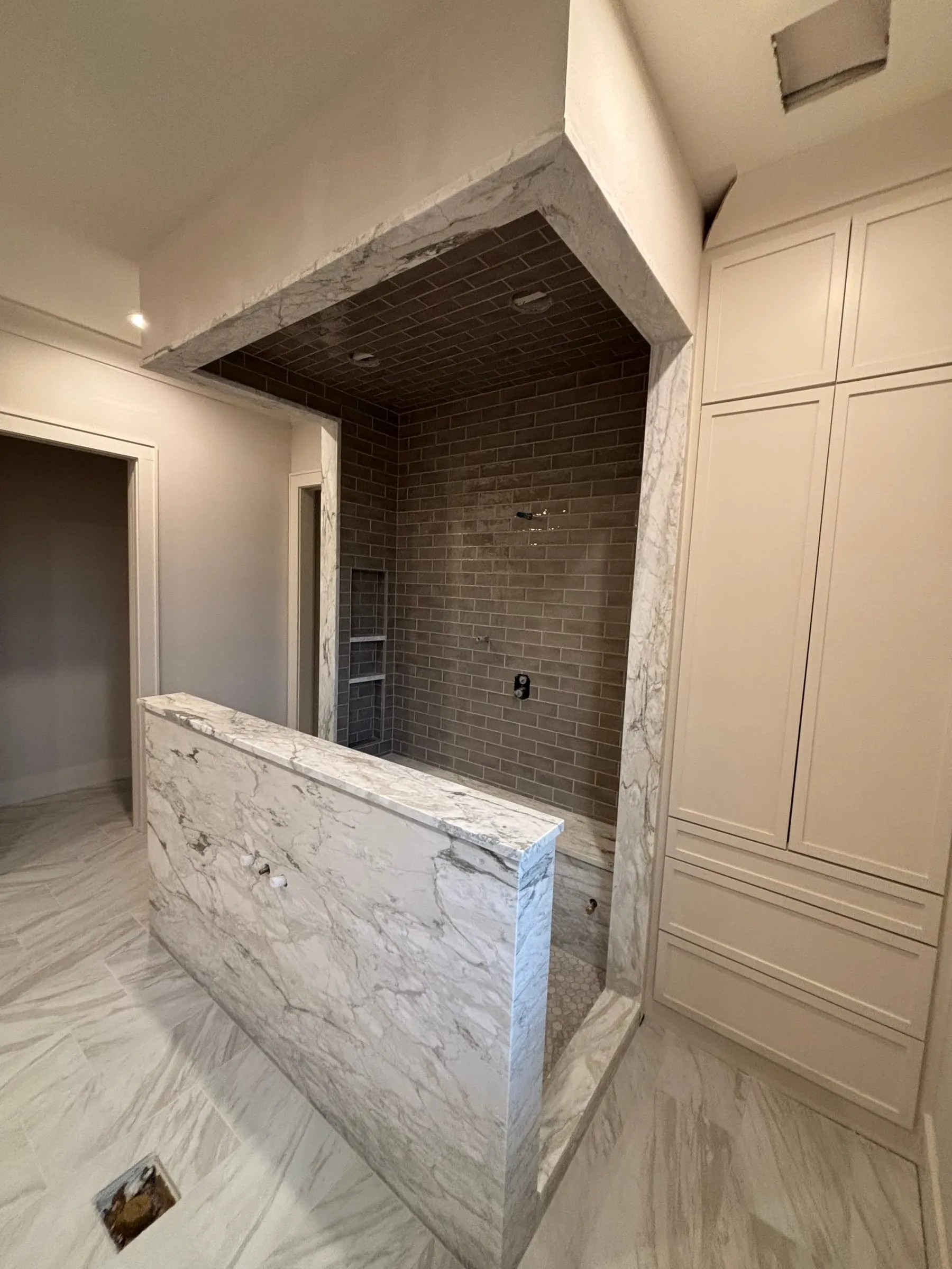 Primary bath with a marble-look half wall and a walk-in shower lined in gray tile, including the ceiling