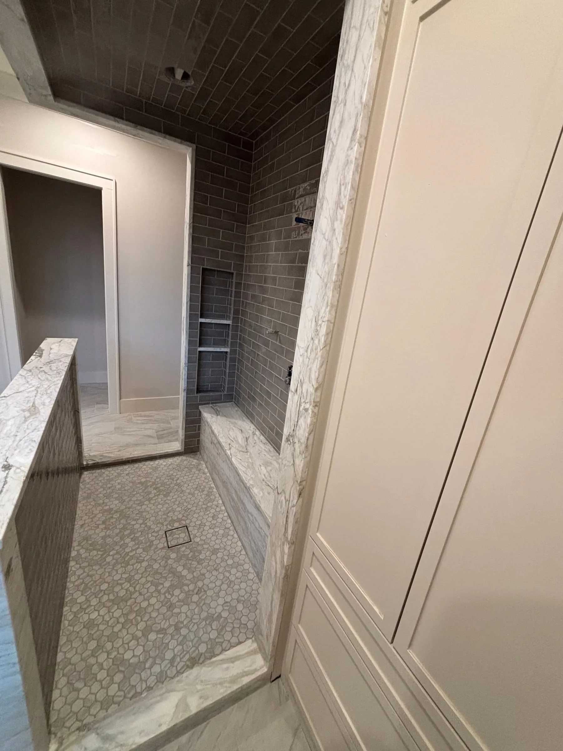 Inside the walk-in shower: gray tile walls and ceiling, a marble-look curb, and a mosaic floor