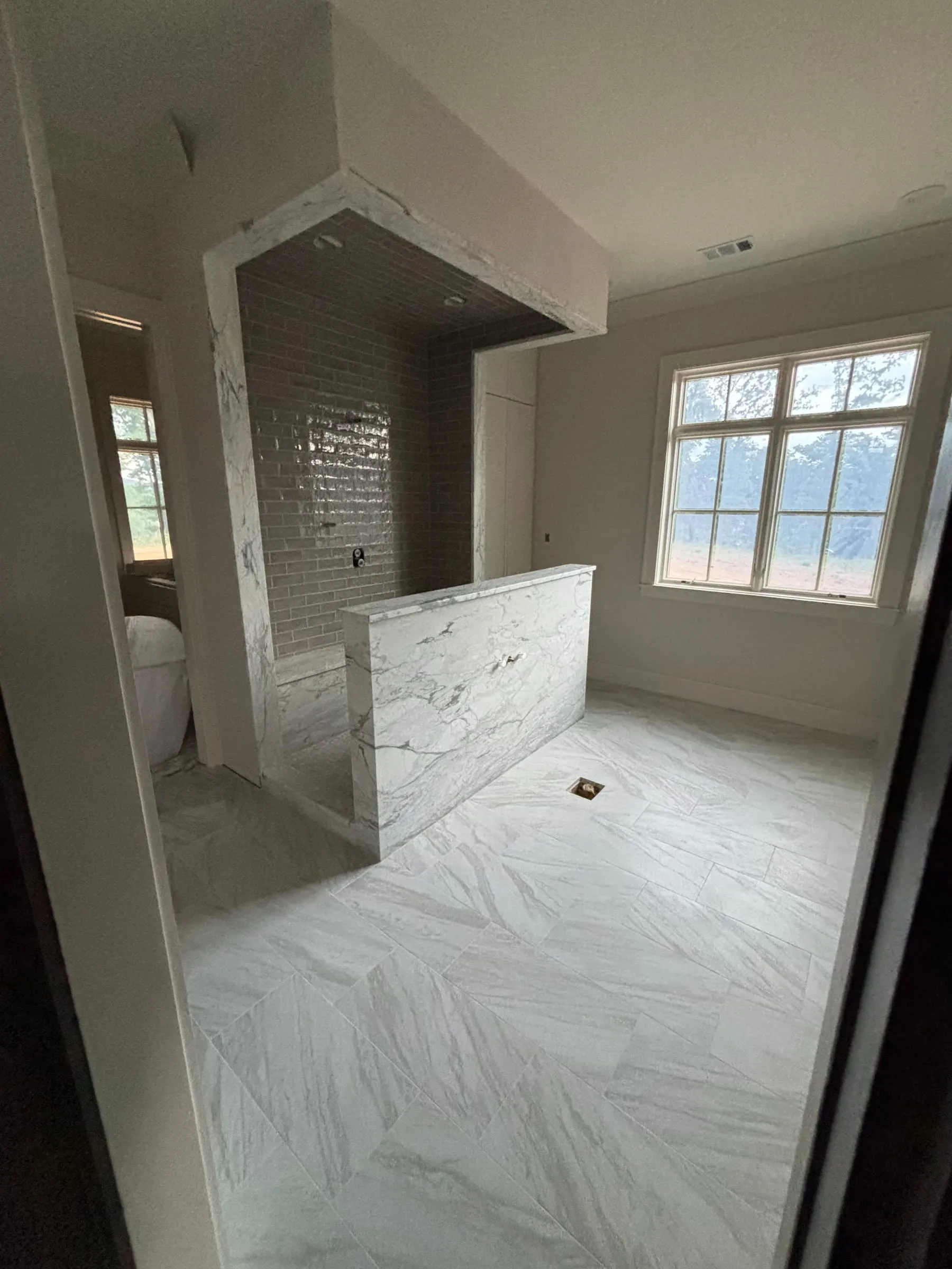 Marble-look floor tile running through the primary bath to the shower half wall