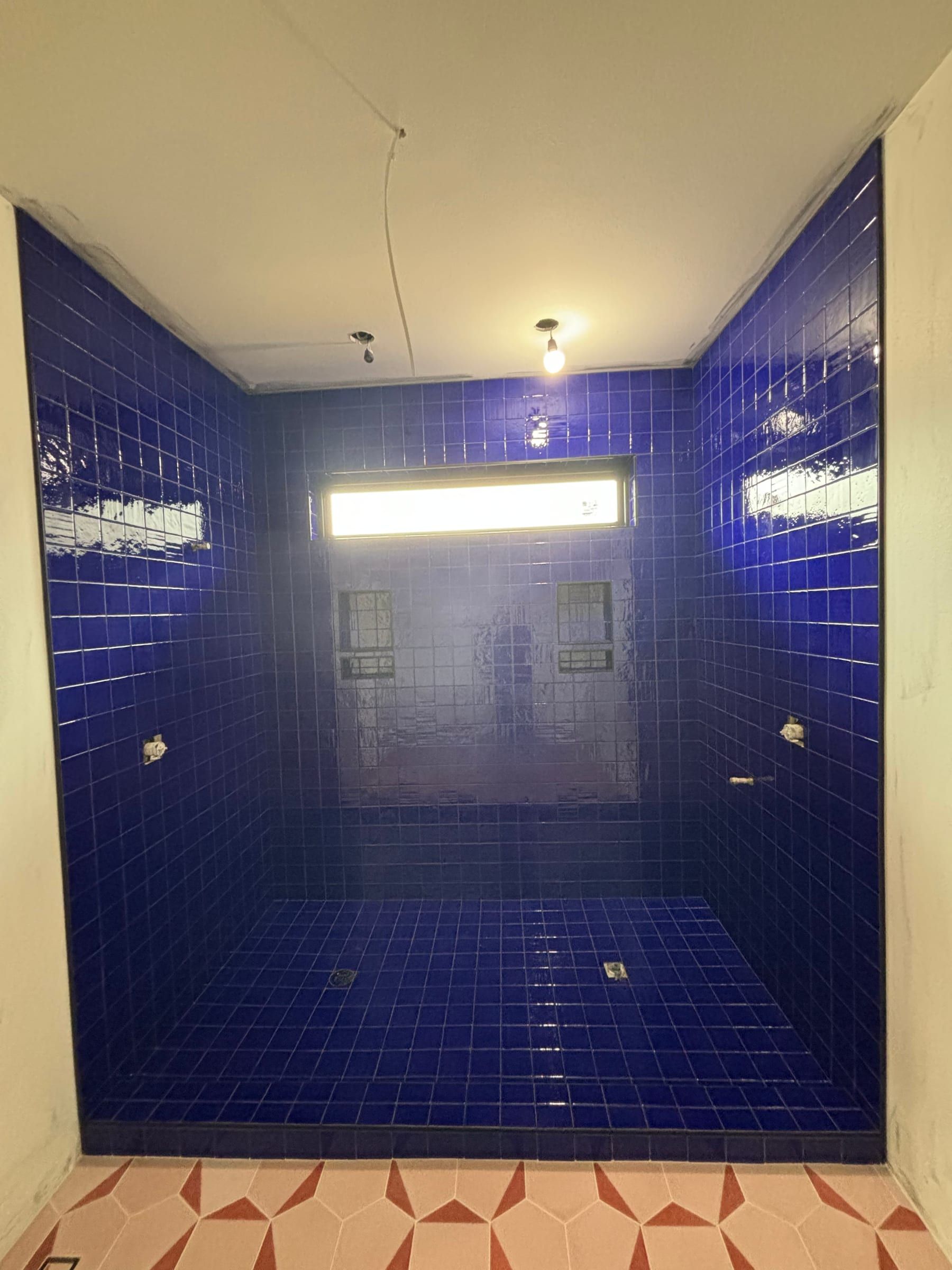 Walk-in shower in glossy cobalt-blue square tile with a pink and white geometric floor