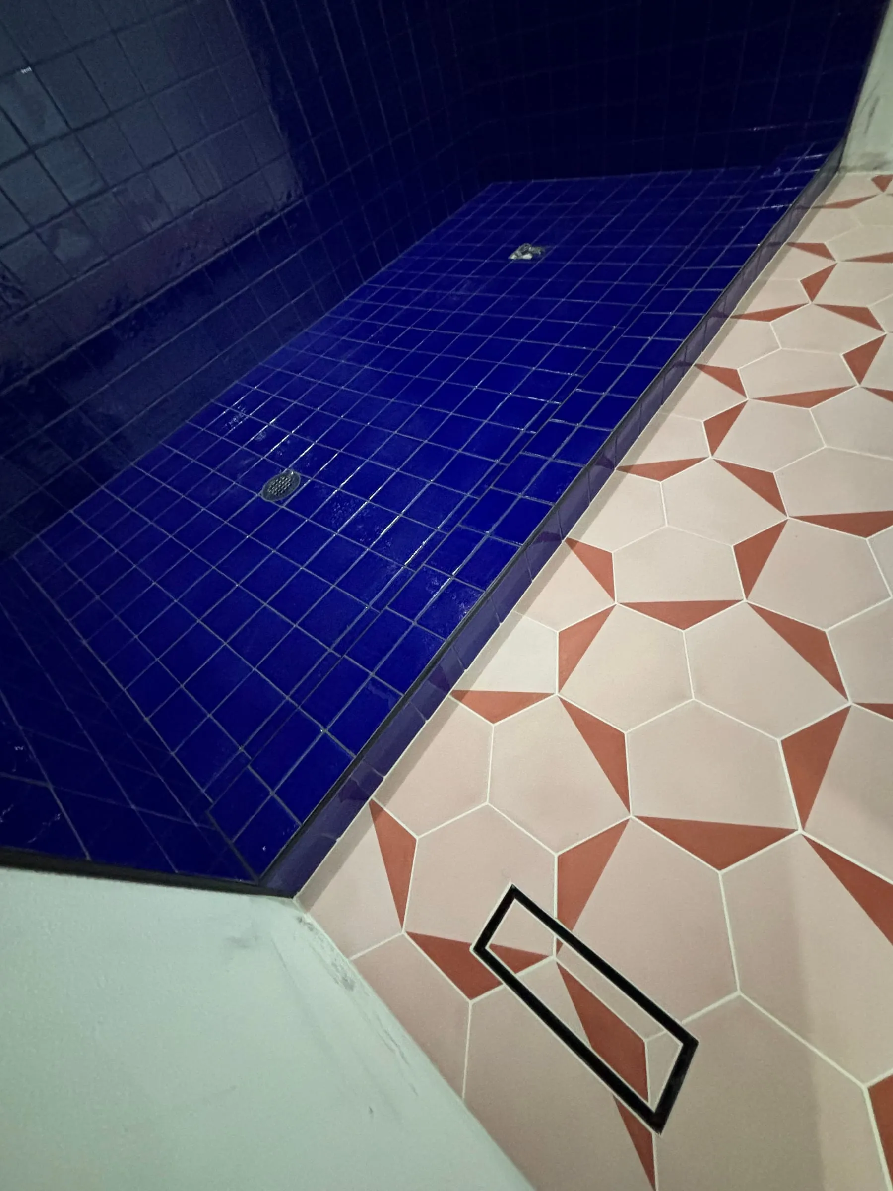Close-up where the cobalt shower meets the pink and white patterned floor