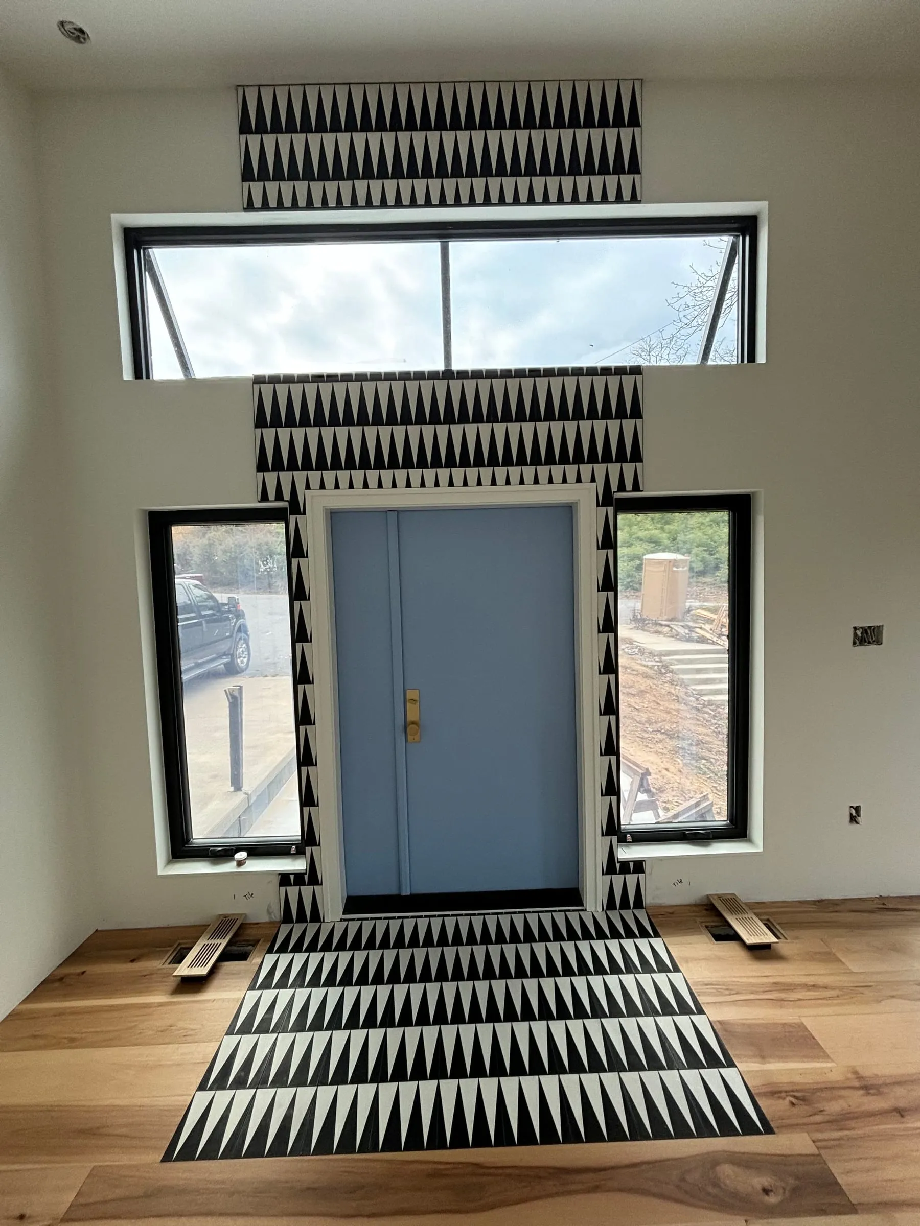 Entry with a black and white triangle-pattern tile rug and matching tile around the front door