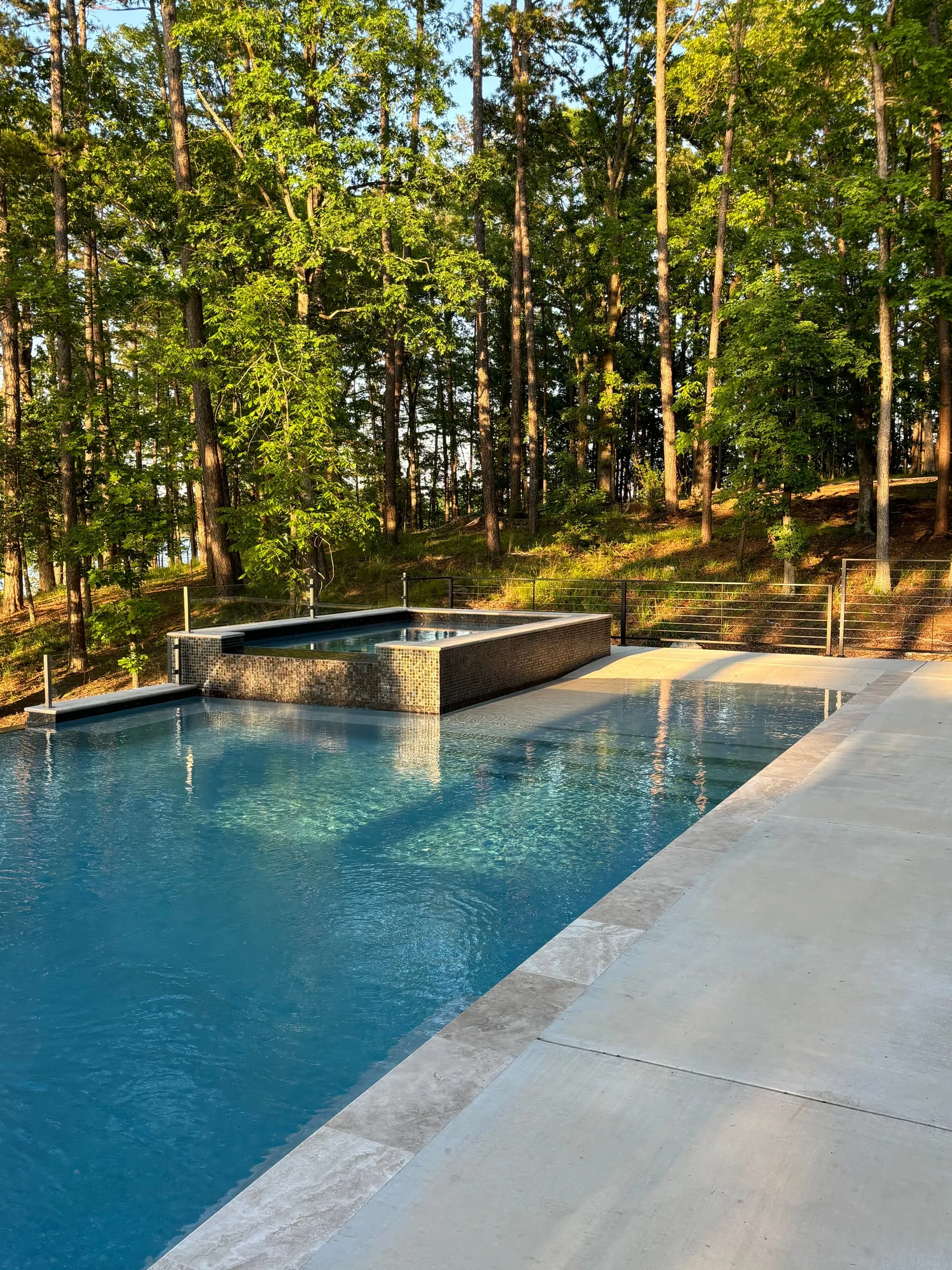 Pool and raised spa with a light coping edge, surrounded by trees
