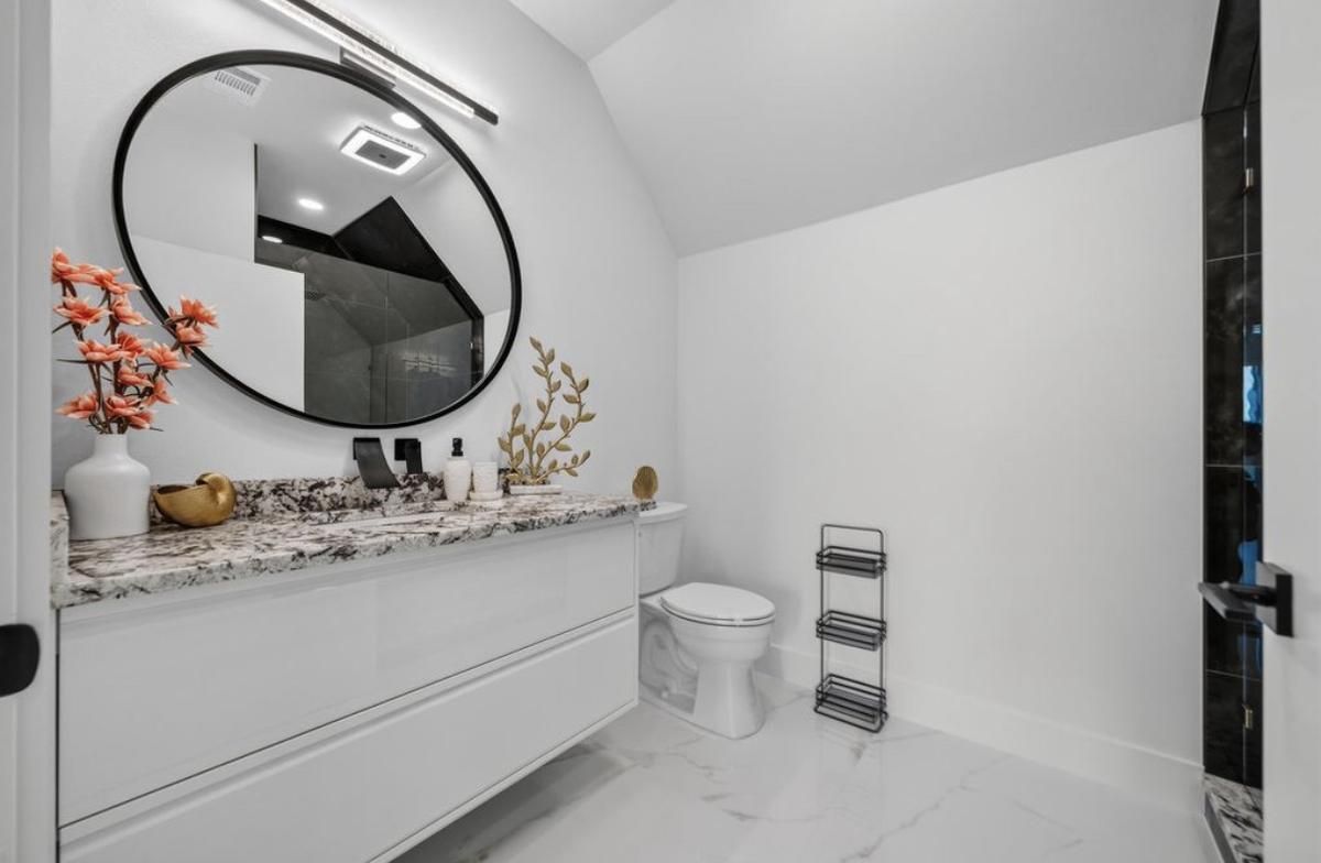Powder room with a floating vanity, round mirror, and white marble-look floor tile