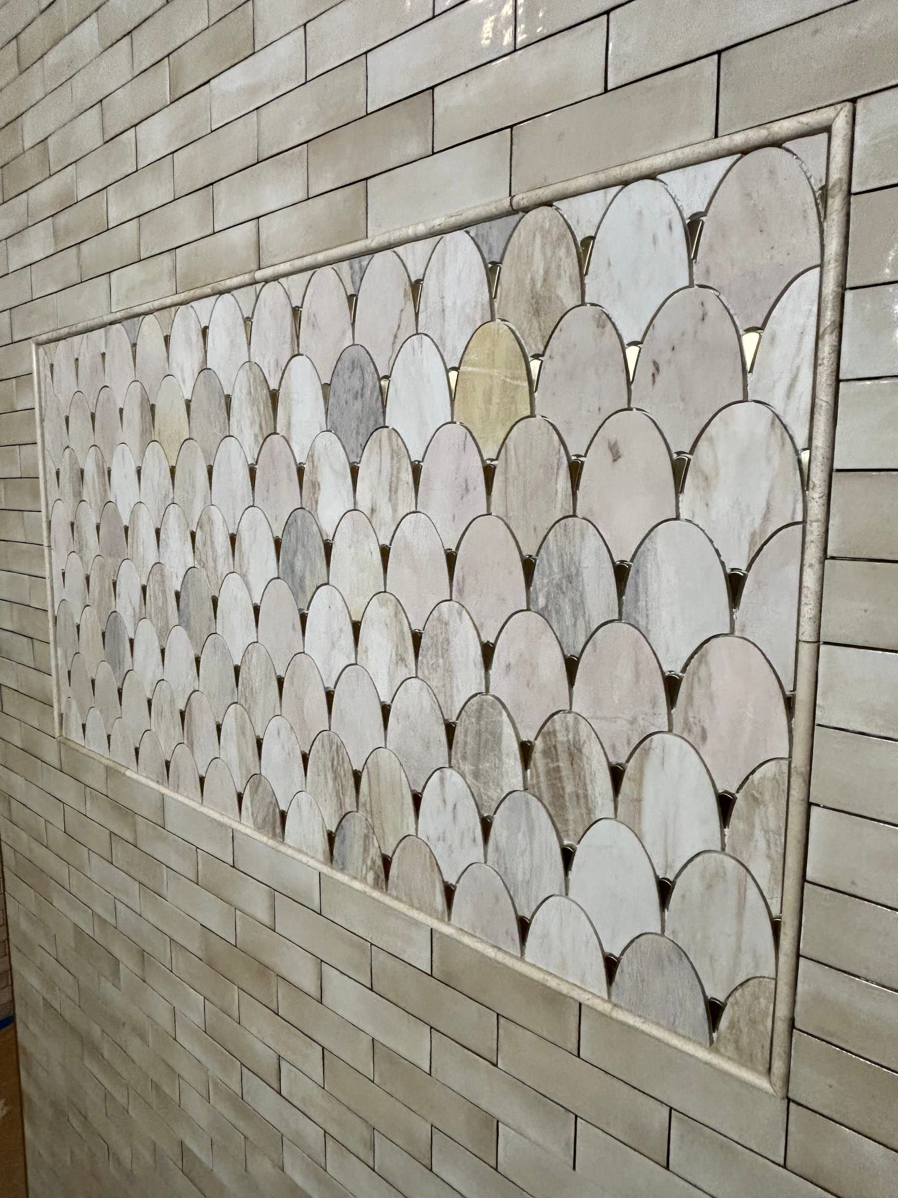 Close-up of a framed marble fish-scale mosaic panel set into cream tile