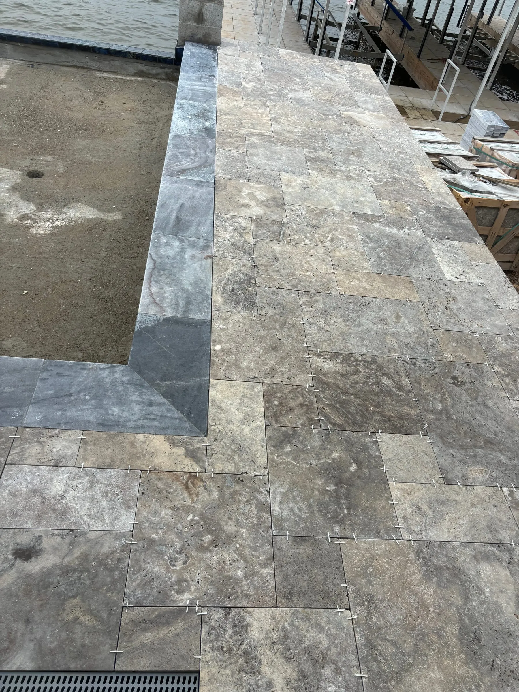 Silver travertine pavers in a French pattern with a stepped coping edge, during installation